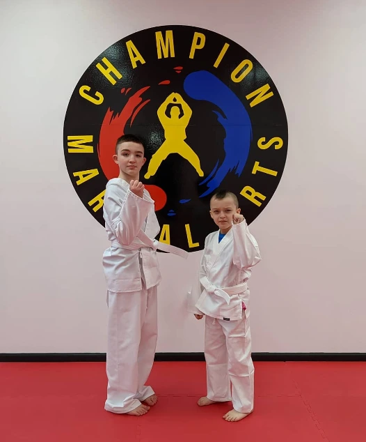 Two students posing in front of the Champion Martial Arts logo