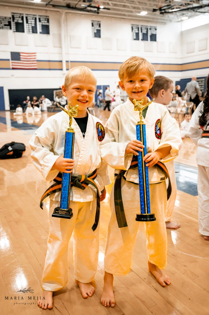 Two young martial arts students holding tournament trophies at Champion Martial Arts