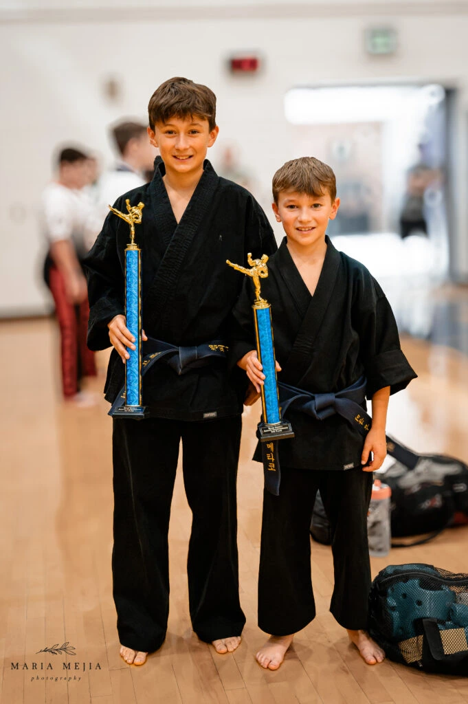 Two martial arts students in black uniforms holding trophies