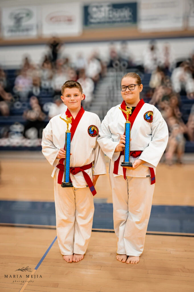 Two Champion Martial Arts students holding trophies in the gym