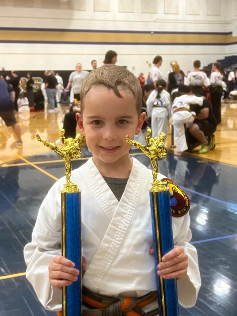Young Champion Martial Arts student holding two tournament trophies