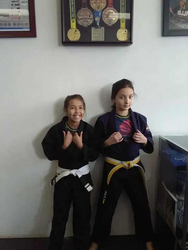 Two youth jiu-jitsu students posing beneath medal displays at Roll Dogs Jiu Jitsu